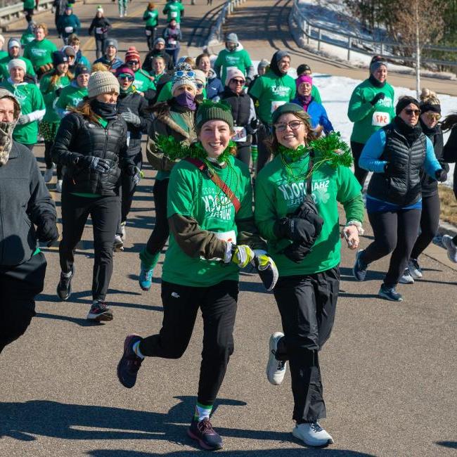 A group participants in a Shamrock Shuffle fundraiser dressed in festive green shirts and accessories showcasing community spirit